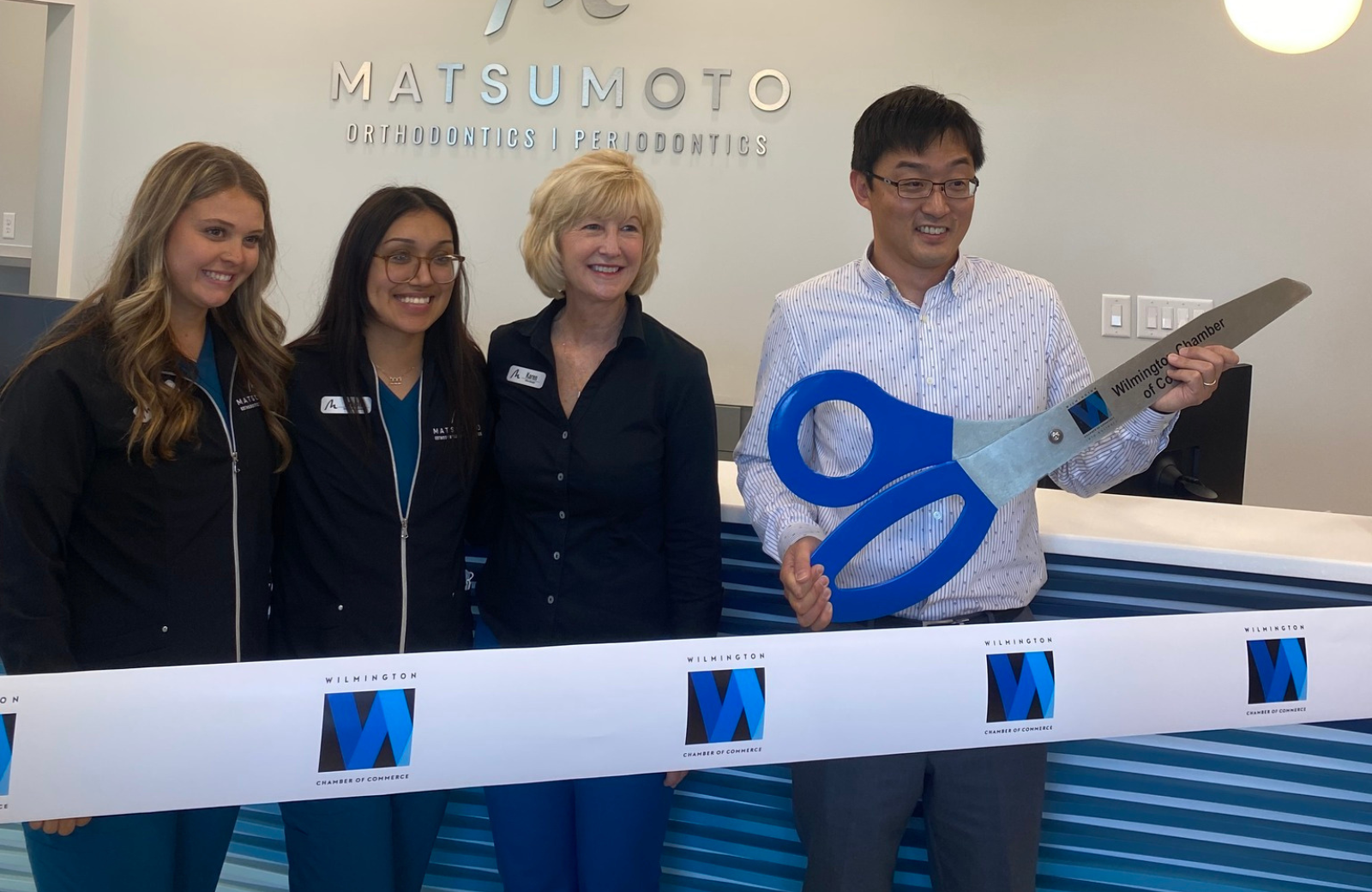 orthodontist matsumoto stands with orthodontic team holding giant scissors for cutting a ribbon