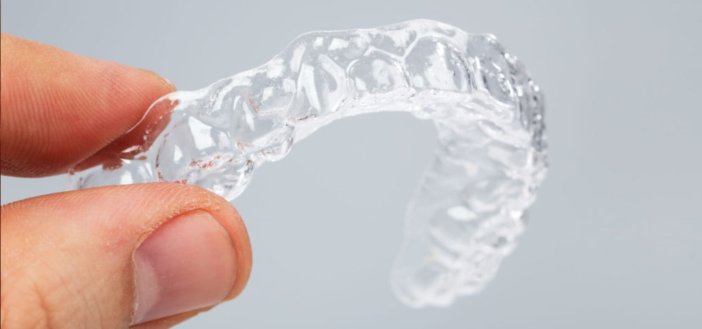 orthodontic patient holds their clean retainer after learning how to clean retainers