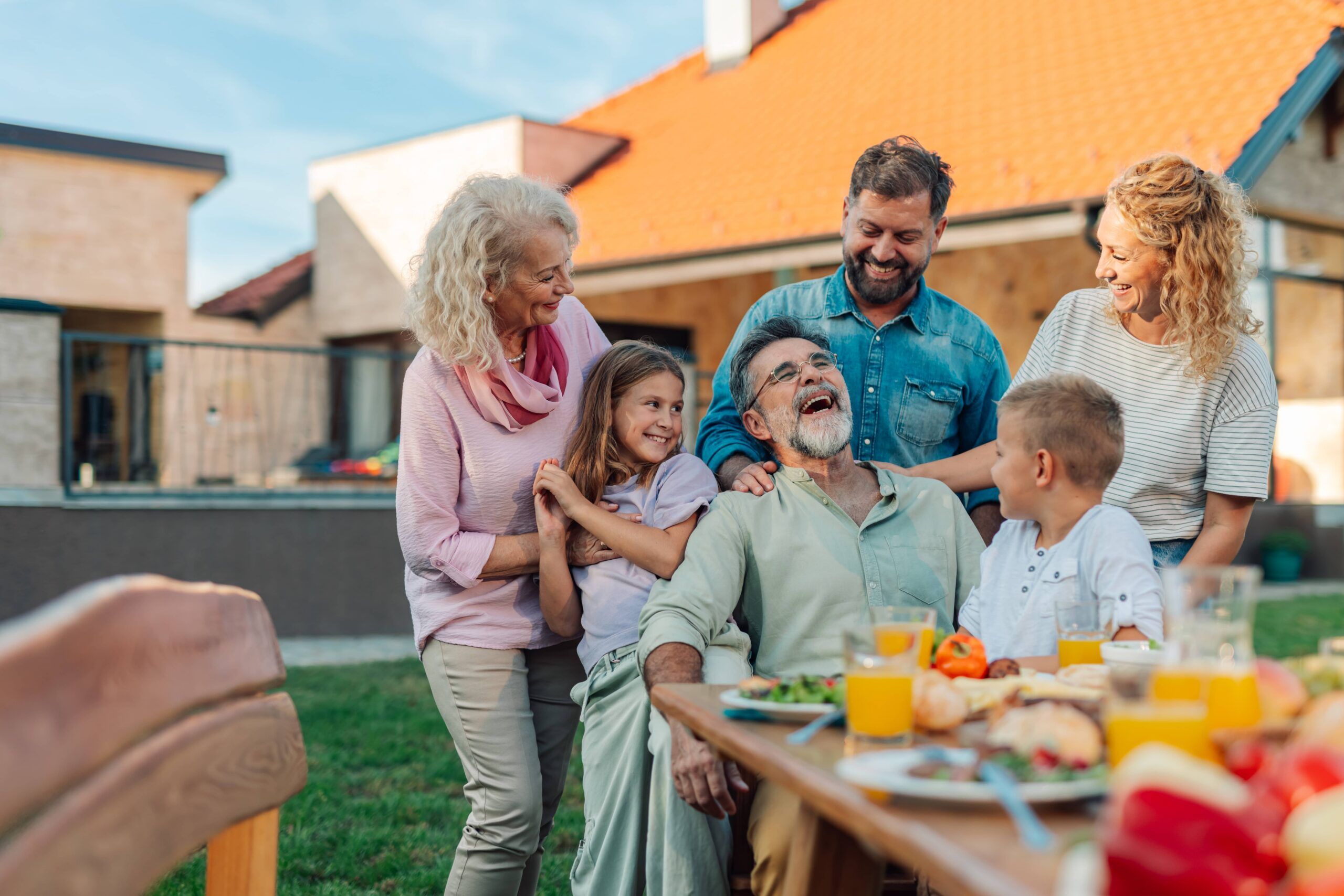 Cheerful multigenerational family, including grandparents, parents, and children, is gathered around an outdoor table