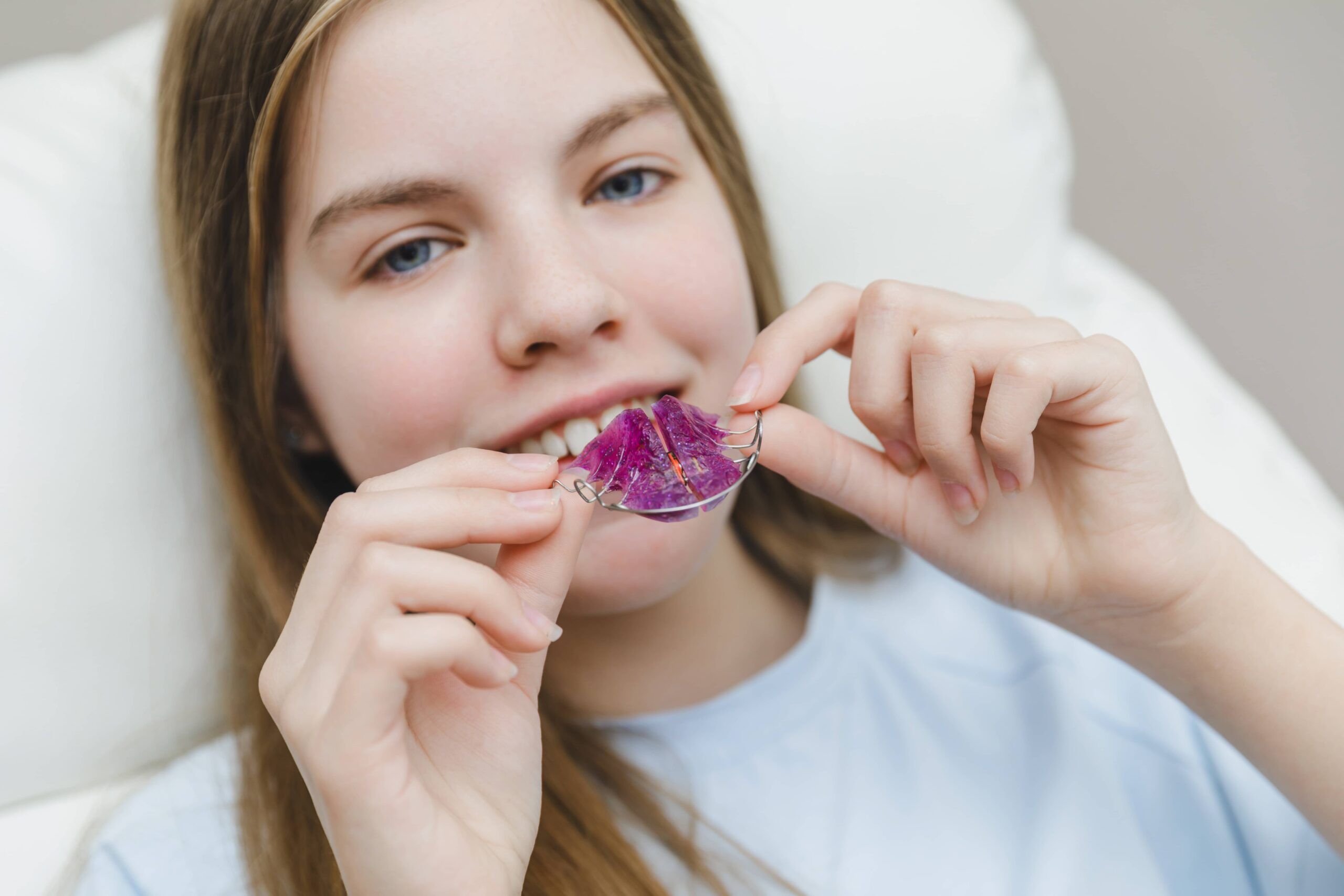 Smiling teenage girl in a dental chair looking at her purple orthodontic plate